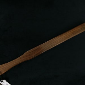 May include: A wooden paddle with a rounded handle and a flat, rectangular blade. The paddle is made of dark brown wood and has a smooth finish.