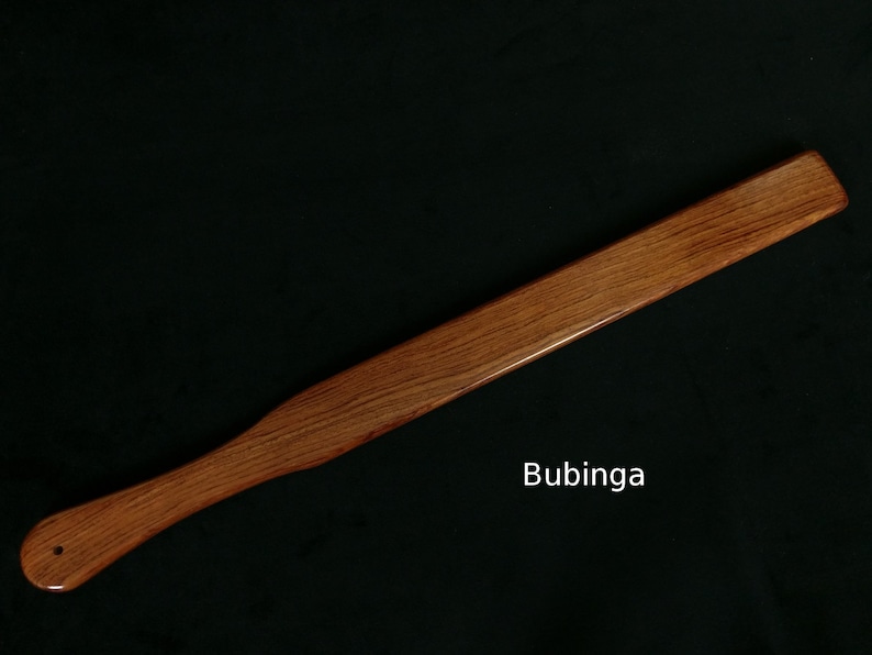 May include: A long, wooden paddle made of bubinga wood. The paddle is smooth and has a rich reddish-brown color.