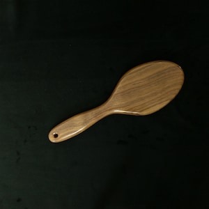 May include: A wooden hairbrush with a brown oval-shaped head and a long, brown handle.
