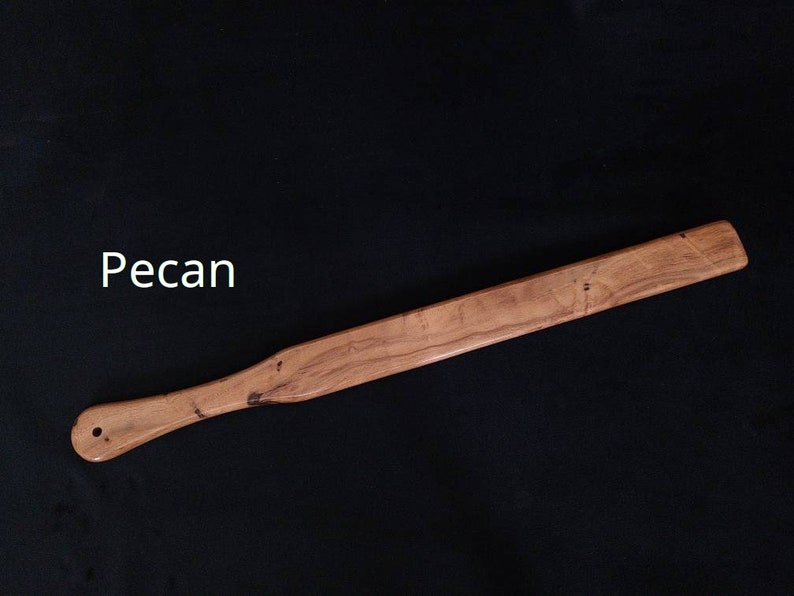 May include: A wooden paddle made from pecan wood. The paddle is light brown in color and has a smooth finish. The paddle is about 18 inches long and has a rounded handle.