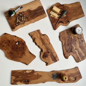 May include: Several wooden chopping boards with organic edges are displayed. Some boards have food items such as cheese, walnuts, and an apple. A tape measure, pencil, and jar are also present, suggesting a rustic, artisanal theme.