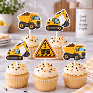 Puede incluir: Cinco cupcakes con decoraciones de construcción sobre palitos blancos. Los adornos incluyen dos camiones volquete amarillos con tierra, dos excavadoras amarillas y una señal triangular naranja y negra que dice BIRTHDAY ZONE.