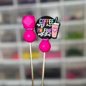 May include: Two decorative picks with bright pink beads and toppers. One pick has a geometric cube and a round bead. The other pick has a black circle with the text "Coffee owns me & I'm fine with that" and a coffee cup graphic.