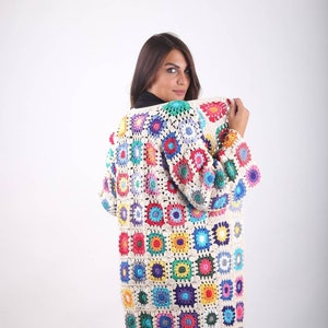 May include: A long, crocheted cardigan with a colourful patchwork design. The cardigan is made of white yarn with squares of different colours, including red, blue, green, yellow, and purple.