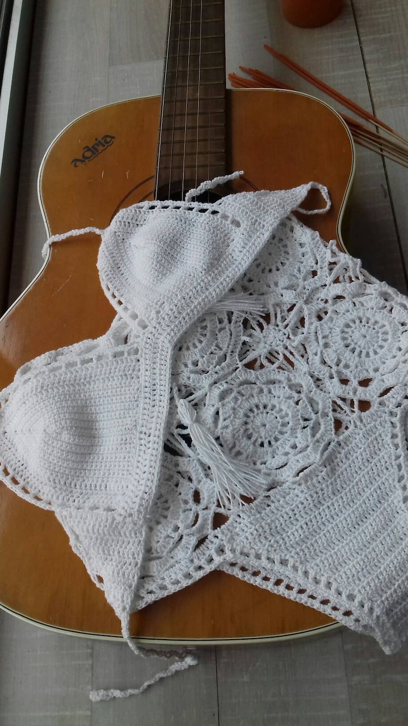 K&ouml;nnte beinhalten: Wei&szlig;es H&auml;keltop mit zartem Blumenmuster und Fransen. Das Top liegt auf einer h&ouml;lzernen Akustikgitarre.