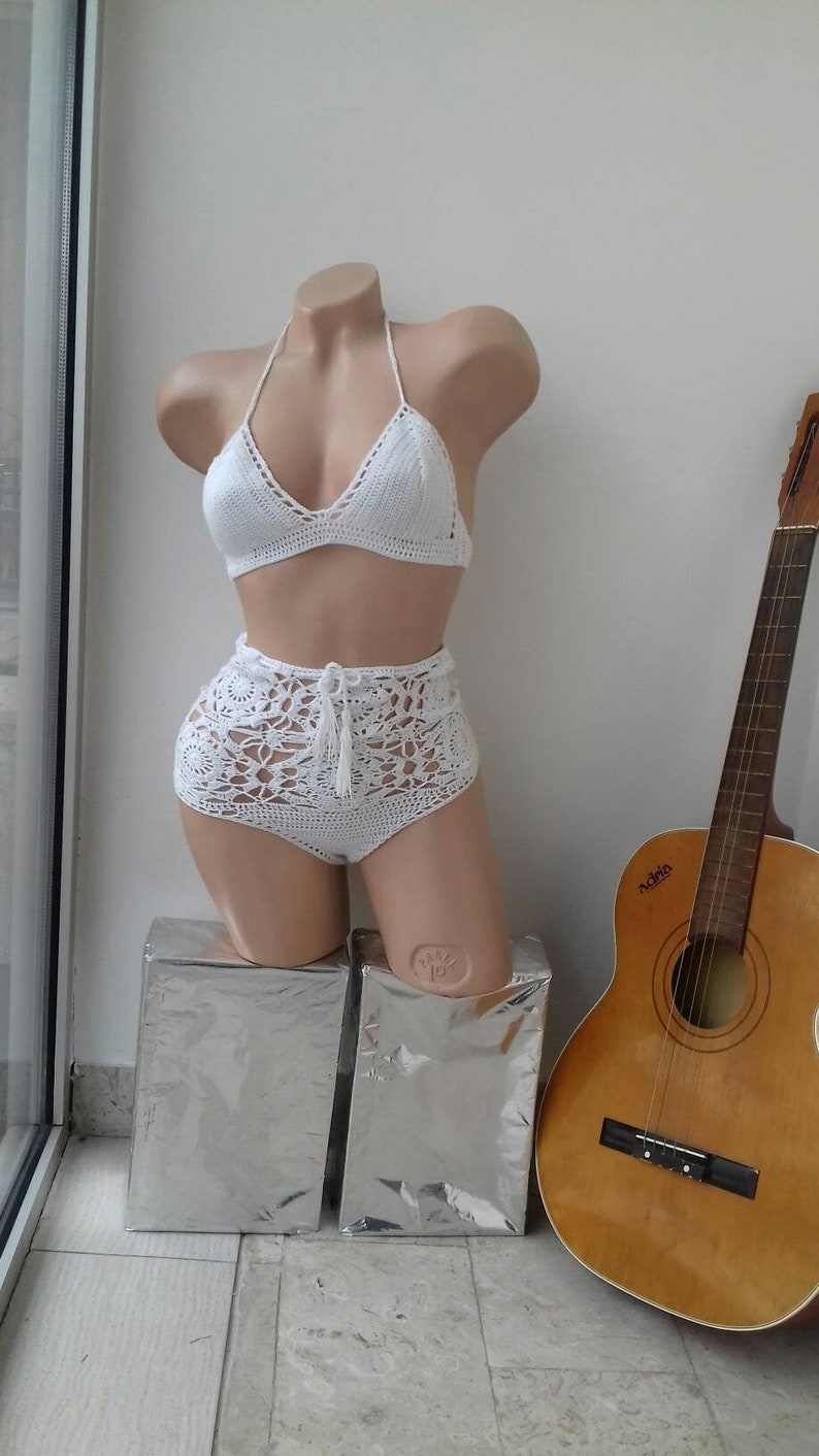 K&ouml;nnte beinhalten: Wei&szlig;er Bikini aus H&auml;kelarbeit mit Oberteil und hoch sitzender Hose. Das Oberteil hat einen Halterneck-Stil mit V-Ausschnitt. Die Hose hat einen hohen Bund und weite Beine.
