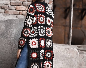 Könnte beinhalten: Ein langer schwarzer Häkelcardigan mit einem farbenfrohen geometrischen Muster. Der Cardigan besteht aus Quadraten mit verschiedenen Farben und Designs, darunter Rot, Weiß, Schwarz und Grün.