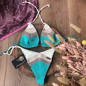 May include: A crocheted bikini top and bottom in turquoise, brown, and white. The bikini is handmade and has a tag that says "Heklani svet".