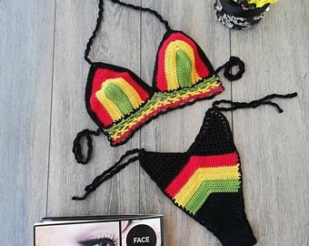 May include: A black crochet bikini top and bottom with red, yellow, and green stripes. The bikini is laid out on a wooden surface.