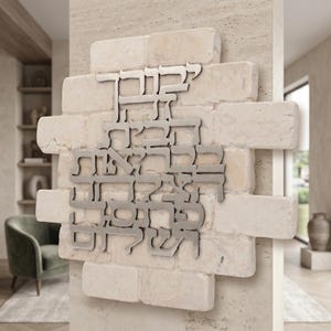 May include: A wall-mounted decorative plaque featuring a rectangular arrangement of light beige, textured stone bricks. Centered on the stone surface is a metallic, silver-toned cutout of Hebrew text, displaying the words Yevarechecha Hashem.