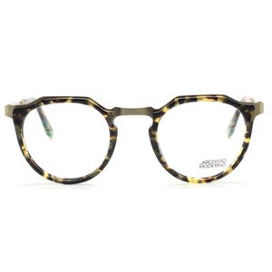 Puede incluir: Gafas redondas con montura con estampado de carey y puente met&aacute;lico fino. Las gafas tienen lentes transparentes y el texto "ARCHIVO MODERNO" es visible en la lente derecha.
