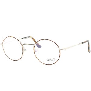 Puede incluir: Gafas redondas con montura fina plateada y estampado carey en los bordes y varillas. Las lentes son transparentes y el texto "ARCHIVO MODERNO" est&aacute; impreso en la lente inferior derecha.