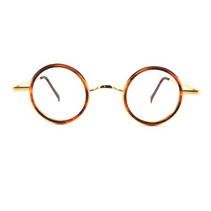 May include: Round eyeglasses with a tortoiseshell pattern on the rims and gold-colored metal arms. The lenses are clear, and the glasses have a classic, vintage style. The frame is a thin, delicate design.