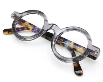 May include: Gray round glasses with tortoise shell arms. The glasses have a clear lens.