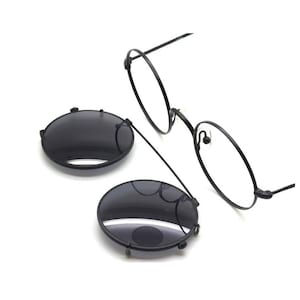 Könnte beinhalten: Schwarze runde Clip-on-Sonnenbrillen mit einem Metallrahmen. Die Sonnenbrille hat ein Federscharnier und ist an einer dünnen Metallkette befestigt.