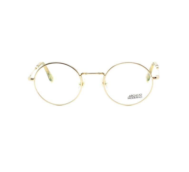 May include: Gold-rimmed eyeglasses with round lenses. The frames are a light gold color, and the lenses are clear. The text "ARCHIVO MODERNO" is printed on the right lens. The glasses have a classic, minimalist design.