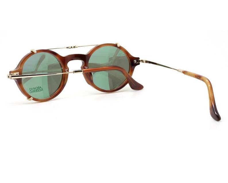 May include: Round brown sunglasses with green lenses. The glasses have a gold-colored bridge and arms, with a tortoiseshell pattern on the earpieces. The lenses have a slight green tint, and the frame is a warm brown color.