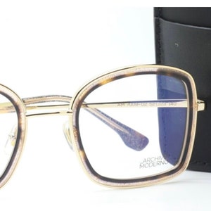 May include: Gold-rimmed eyeglasses with a tortoise shell frame and blue tinted lenses. The glasses are shown with a black leather case with the text "ARCHIVES MODERN" on it.