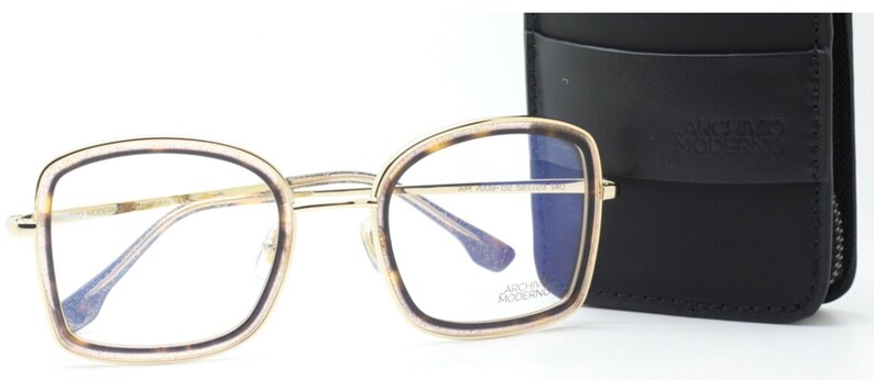 May include: Gold-rimmed eyeglasses with a tortoise shell frame and blue tinted lenses. The glasses are shown with a black leather case with the text "ARCHIVES MODERN" on it.