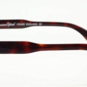 Puede incluir: Un par de gafas de pasta de carey con montura de metal plateado. Las gafas tienen forma redonda y las patillas son de pl&aacute;stico de carey. El nombre de la marca "High American Optical" est&aacute; impreso en la patilla.