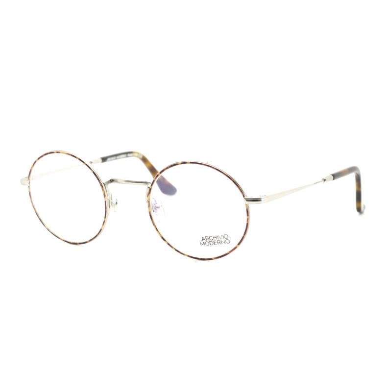 Puede incluir: Gafas redondas con montura fina plateada y estampado carey en los bordes y varillas. Las lentes son transparentes y el texto "ARCHIVO MODERNO" est&aacute; impreso en la lente inferior derecha.