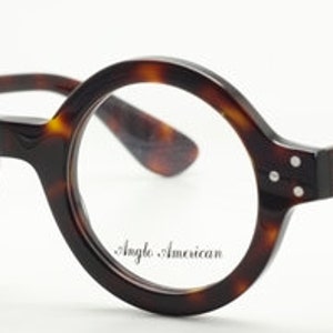 Puede incluir: Gafas redondas de carey con montura negra y lentes transparentes. El nombre de la marca "Angle. American" est&aacute; impreso en la lente derecha.