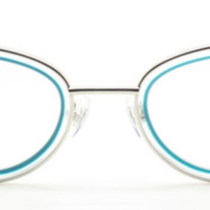 May include: Silver cat-eye glasses with a blue trim and the text "Archivo Moderno" on the right lens.