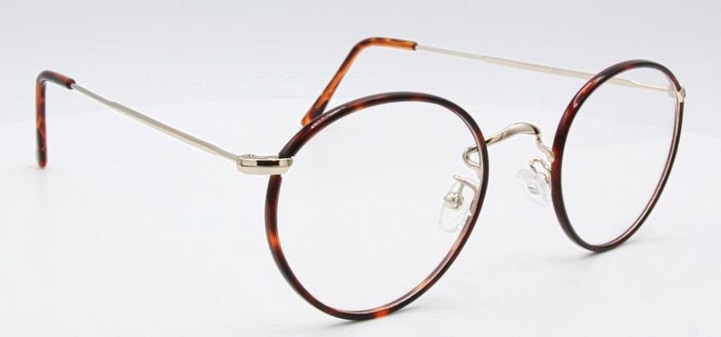 May include: Round eyeglasses with a tortoiseshell pattern on the rims and temples. The frames have a silver-colored bridge and arms. The lenses are clear. The glasses are set against a white background.