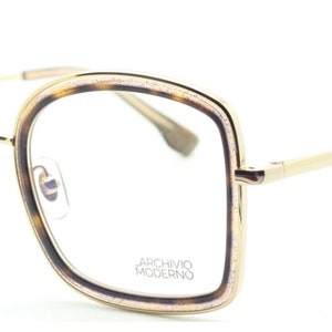 May include: Gold-rimmed eyeglasses with a tortoise shell frame and clear lenses. The frame has a subtle sparkle and the brand name "Archivio Moderno" is printed on the right lens.