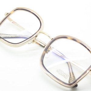 May include: Gold and tortoise shell eyeglasses with square frames and clear lenses. The brand name "Archivo Moderno" is printed on the right lens.