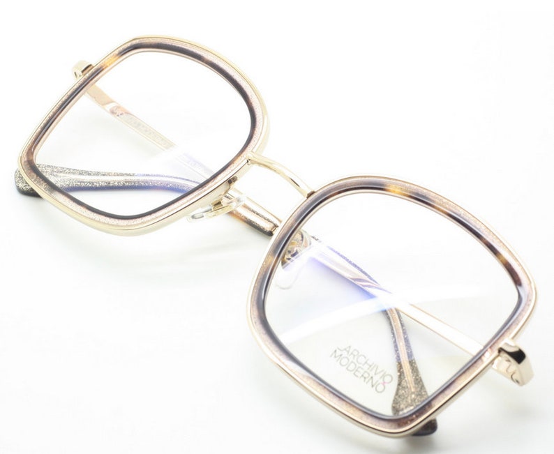 May include: Gold and tortoise shell eyeglasses with square frames and clear lenses. The brand name "Archivo Moderno" is printed on the right lens.