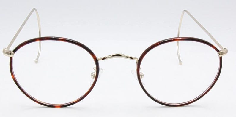 May include: Round eyeglasses with a tortoiseshell pattern on the frames. The glasses have a silver bridge and temples, and clear lenses. The design is classic and elegant, suitable for everyday wear.