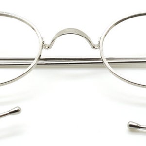 May include: Silver round eyeglasses with a thin metal frame and spring hinges. The temples are made of a thin metal wire that wraps around the ear.