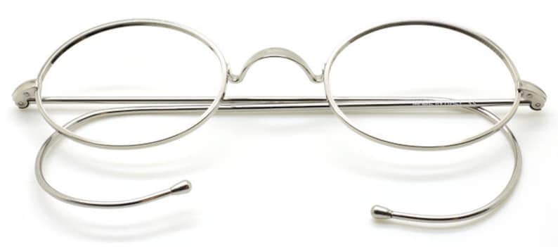 May include: Silver round eyeglasses with a thin metal frame and spring hinges. The temples are made of a thin metal wire that wraps around the ear.