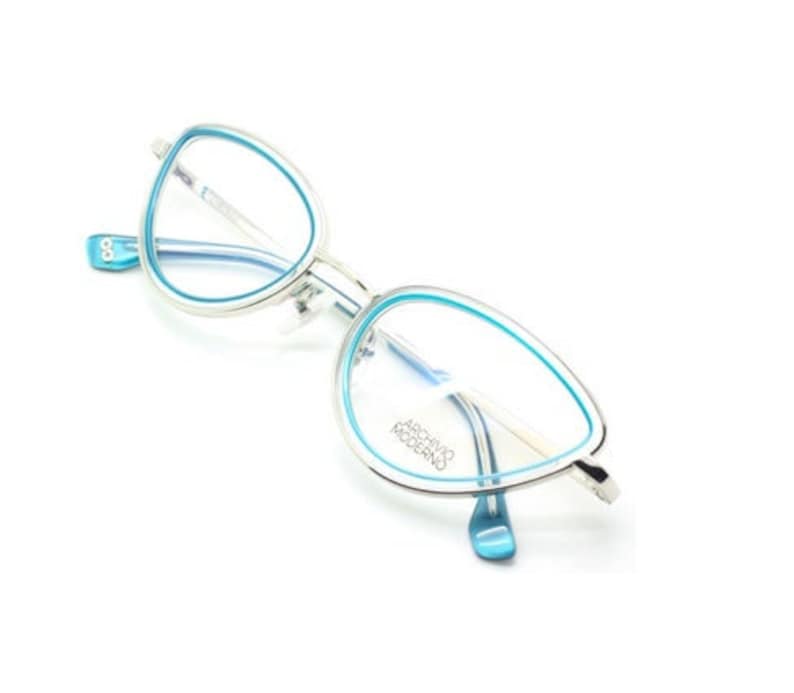 May include: Silver cat-eye glasses with blue frames and clear lenses. The brand name "ARCHIVIO MODERNO" is printed on the right lens.