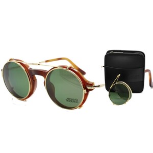May include: Round brown and gold-rimmed sunglasses with green lenses. The sunglasses have a double bridge and a small, round, foldable pair. A black leather case is also included. The text "ARCHIVO MODERNO" is visible on the lens.