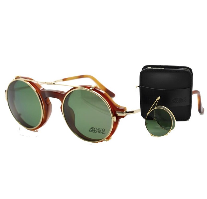 May include: Round brown and gold-rimmed sunglasses with green lenses. The sunglasses have a double bridge and a small, round, foldable pair. A black leather case is also included. The text "ARCHIVO MODERNO" is visible on the lens.