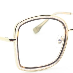 May include: Gold-tone eyeglasses with a square frame and clear lenses. The frame has a subtle sparkle detail.