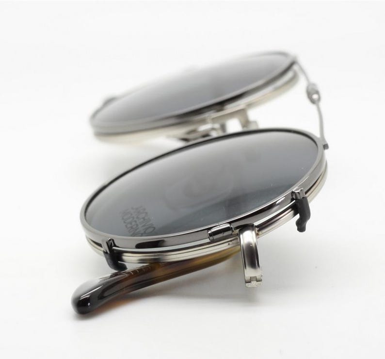 Puede incluir: Primer plano de unas gafas de sol redondas con lentes oscuras y montura plateada. Las patillas tienen un dise&ntilde;o de carey. El texto "ARCHIVO MODERNO" es visible.
