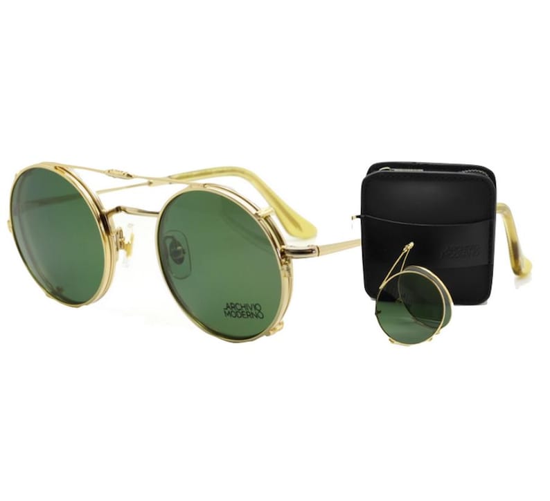 May include: Gold-rimmed sunglasses with green lenses and a matching case. The sunglasses have a double bridge and round lenses. The case is black and rectangular. The text "ARCHIVO MODERNO" is visible on the lens.