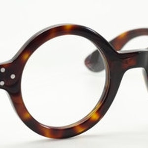 Puede incluir: Gafas redondas de pasta de carey con lentes transparentes. La montura tiene un sutil patr&oacute;n de carey y las lentes son transparentes. El nombre de la marca "Angle America" est&aacute; impreso en la lente derecha.