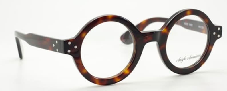 Puede incluir: Gafas redondas de pasta de carey con lentes transparentes. La montura tiene un sutil patr&oacute;n de carey y las lentes son transparentes. El nombre de la marca "Angle America" est&aacute; impreso en la lente derecha.