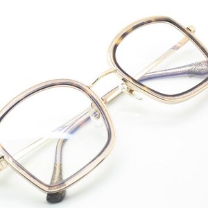 May include: Gold-rimmed square eyeglasses with a tortoise shell pattern on the frame. The glasses have clear lenses.