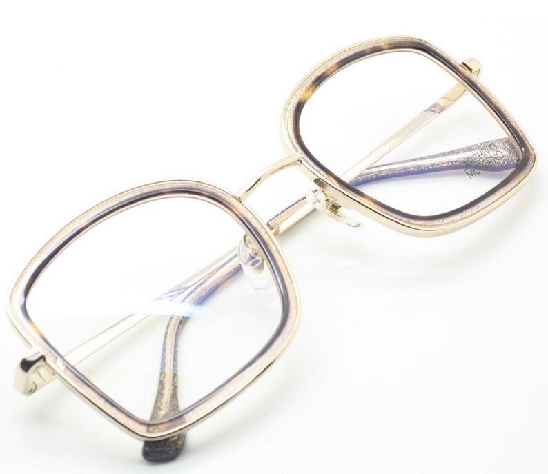 May include: Gold-rimmed square eyeglasses with a tortoise shell pattern on the frame. The glasses have clear lenses.