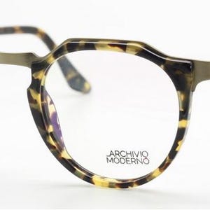 Puede incluir: Gafas redondas con montura y patillas con estampado de carey. Las monturas tienen una forma geom&eacute;trica &uacute;nica. Las lentes son transparentes y el puente y las bisagras son de color dorado apagado. El texto "ARCHIVO MODERNO" est&aacute; impreso en la lente.