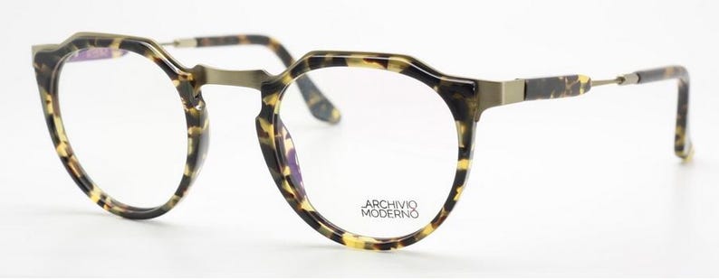 Puede incluir: Gafas redondas con montura y patillas con estampado de carey. Las monturas tienen una forma geom&eacute;trica &uacute;nica. Las lentes son transparentes y el puente y las bisagras son de color dorado apagado. El texto "ARCHIVO MODERNO" est&aacute; impreso en la lente.