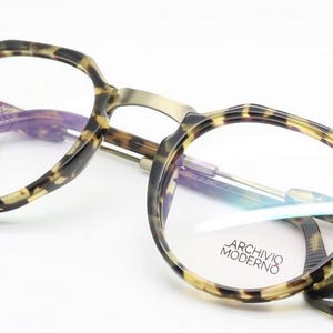 Puede incluir: Gafas redondas con montura y patillas con estampado de carey. El puente y las varillas son de color dorado met&aacute;lico. El texto "ARCHIVO MODERNO" est&aacute; impreso en la lente derecha.