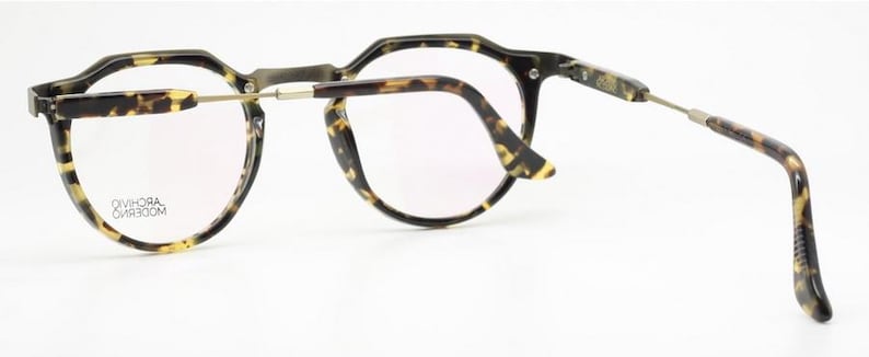 Puede incluir: Gafas con montura y patillas con estampado de carey. Las lentes son transparentes y las monturas tienen un dise&ntilde;o angular &uacute;nico. Las patillas est&aacute;n conectadas a las monturas con bisagras plateadas. El texto "DIVHORA MODERN" est&aacute; impreso en la lente.