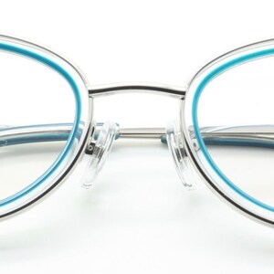 May include: Silver cat-eye glasses with a light blue trim. The glasses have a clear lens and the brand name "Archivio Moderno" is printed on the right temple.