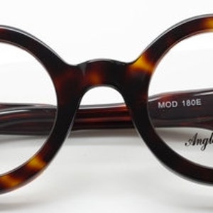 Puede incluir: Gafas redondas de carey con lentes transparentes. Las monturas tienen un sutil patr&oacute;n marr&oacute;n y negro. El nombre de la marca "Anglo American" est&aacute; impreso en la lente derecha y "MOD 180E" y "46D26" est&aacute;n impresos en la patilla derecha.